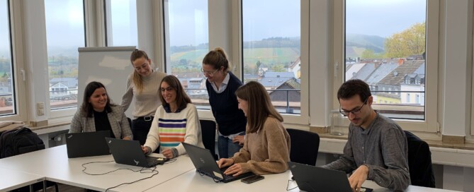 Mehrere Personen versammeln sich um einen Tisch mit ihren Laptops und diskutieren miteinander.